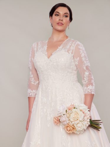 Bride holding flowers wearing bridal gown with beaded lace long sleeves.